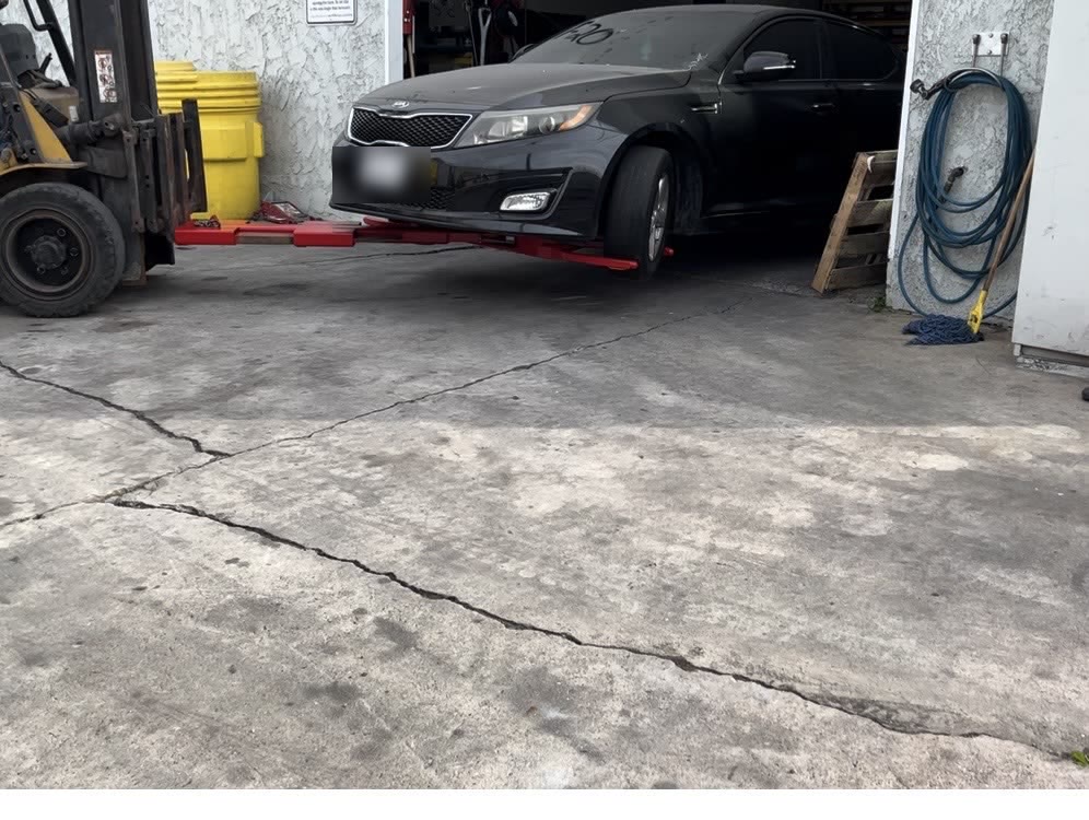 Forklift holding a sedan on the Autowlift beside a shop roll-up door