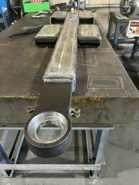 A welded Autowlift lift arm and its machined bearing housing laid out on the fabrication table